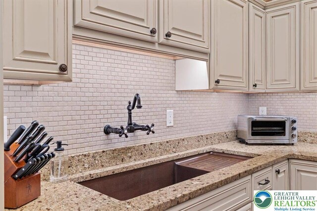 127 Timber Lake Dr, Barrett Twp, PA 18325 - kitchen with backsplash, a sink, cream cabinets, and light stone counters