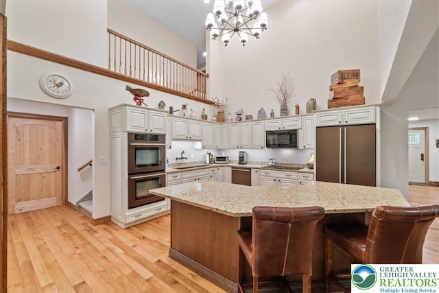 127 Timber Lake Dr, Barrett Twp, PA 18325 - kitchen featuring a towering ceiling, black appliances, a sink, a chandelier, and light wood finished floors