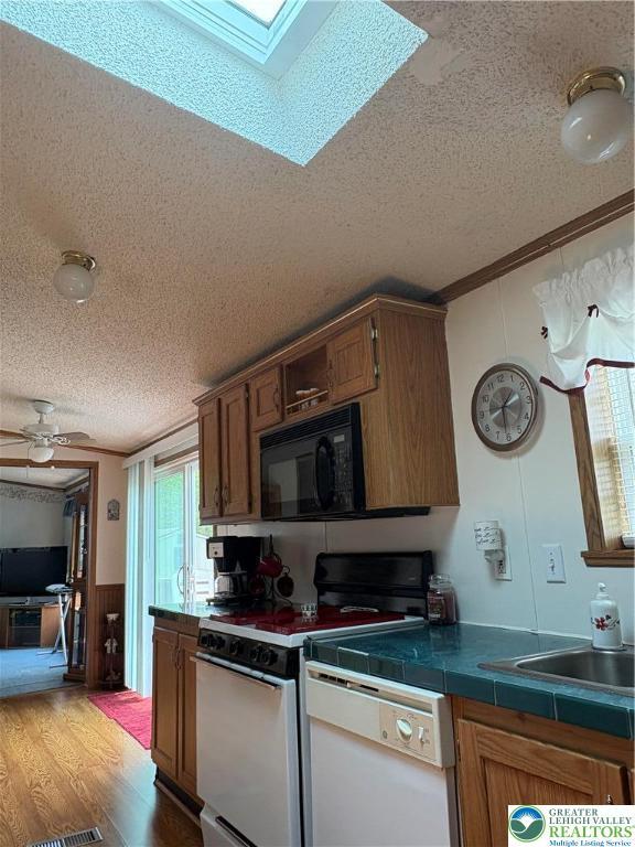 10188 Cork Ln, Upper Macungie Twp, PA 18031 - kitchen featuring white appliances, a textured ceiling, a skylight, brown cabinets, and a wainscoted wall