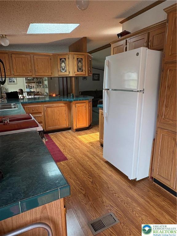 10188 Cork Ln, Upper Macungie Twp, PA 18031 - kitchen featuring freestanding refrigerator, light wood finished floors, a skylight, brown cabinets, and a textured ceiling