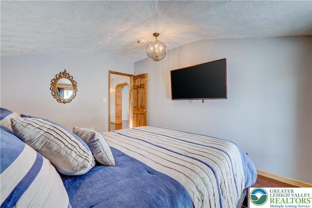 143 Cathleen Dr, Price Twp, PA 18302 - bedroom featuring a textured ceiling, wood finished floors, lofted ceiling, arched walkways, and a chandelier