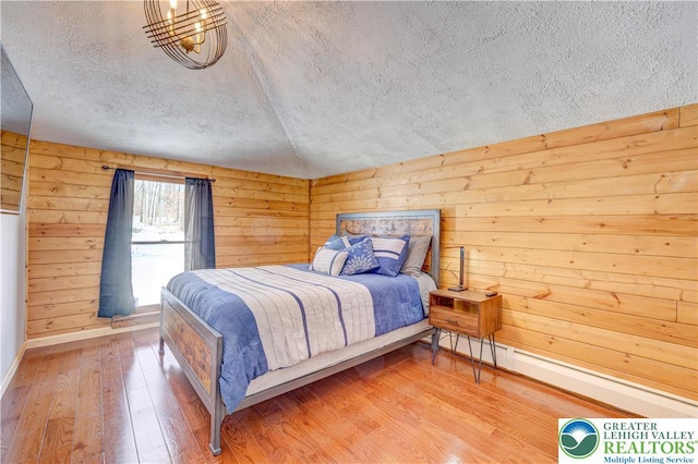 143 Cathleen Dr, Price Twp, PA 18302 - bedroom with a textured ceiling, wood finished floors, a baseboard heating unit, and wood walls