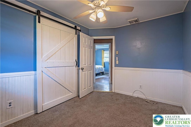 1421 7th St, Bethlehem Twp, PA 18020 - unfurnished bedroom with a barn door, wainscoting, carpet floors, and a ceiling fan
