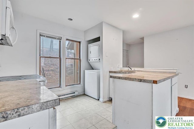 417 Hickory Dr, Jackson Twp, PA 18372 - kitchen featuring stacked washing machine and dryer, white microwave, white cabinets, a baseboard heating unit, and a peninsula