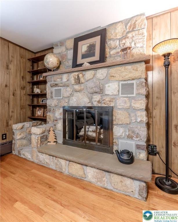 1571 Penn Dr, West Penn Twp, PA 18211 - detailed view of a stone fireplace, wooden walls, wood finished floors, and a baseboard radiator