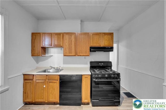 834 Bushkill St, Easton, PA 18042 - kitchen featuring black appliances, under cabinet range hood, light wood-style floors, light countertops, and a wainscoted wall