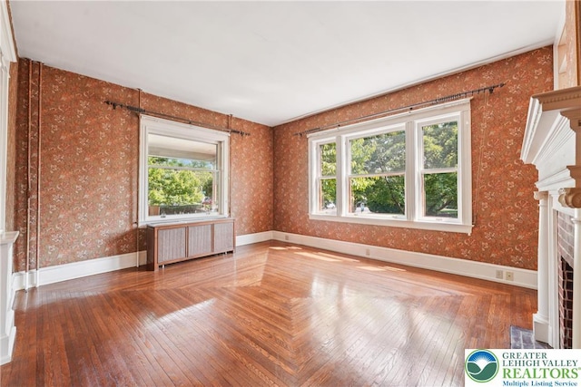 200 W Pierce St, Easton, PA 18042 - unfurnished living room featuring radiator heating unit, plenty of natural light, a fireplace with flush hearth, wallpapered walls, and hardwood / wood-style flooring
