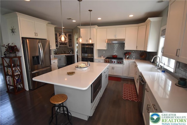 4323 Saratoga Dr, Lower Nazareth Twp, PA 18020 - kitchen featuring stainless steel appliances, under cabinet range hood, a center island, dark wood-style flooring, and tasteful backsplash