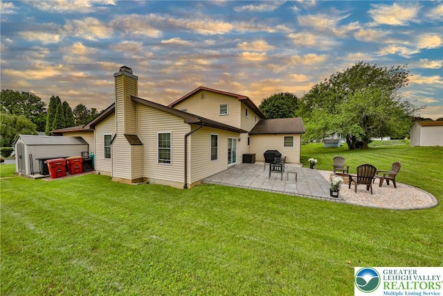 106 Fernwood Dr, Forks Twp, PA 18040 - back of property at dusk featuring a patio, a chimney, a storage shed, a lawn, and an outdoor fire pit