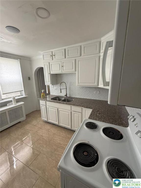 314 S Saint Cloud St, Allentown City, PA 18104 - kitchen with white electric stove, radiator heating unit, arched walkways, white cabinets, and backsplash