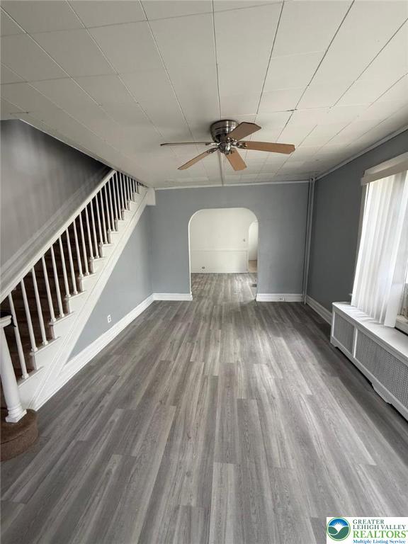 314 S Saint Cloud St, Allentown City, PA 18104 - unfurnished living room with ceiling fan, arched walkways, stairway, wood finished floors, and radiator heating unit