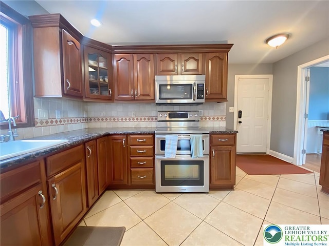 5545 Roberts Rd, North Whitehall Twp, PA 18078 - kitchen featuring appliances with stainless steel finishes, tasteful backsplash, glass insert cabinets, dark stone counters, and light tile patterned flooring