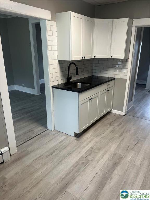 827 Louis St, Easton, PA 18042 - kitchen with white cabinetry, light wood-style floors, decorative backsplash, and dark countertops