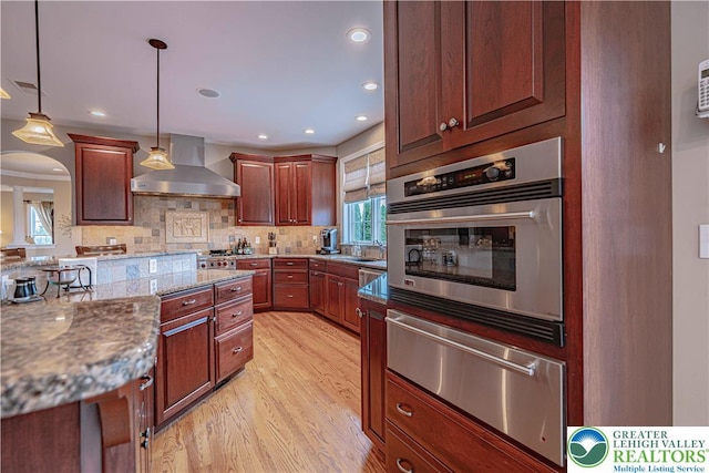 6532 Forest Knoll Ct, Upper Macungie Twp, PA 18106 - kitchen with a warming drawer, wall chimney exhaust hood, light wood-type flooring, decorative backsplash, and hanging light fixtures