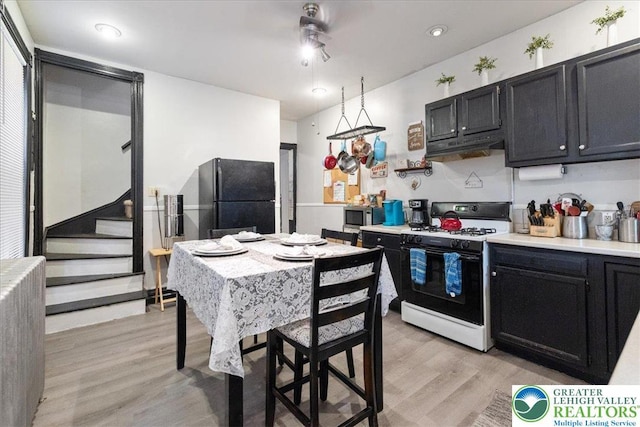 519 N 8th St, Allentown City, PA 18102 - kitchen featuring white range with gas stovetop, freestanding refrigerator, light wood-style floors, dark cabinets, and light countertops