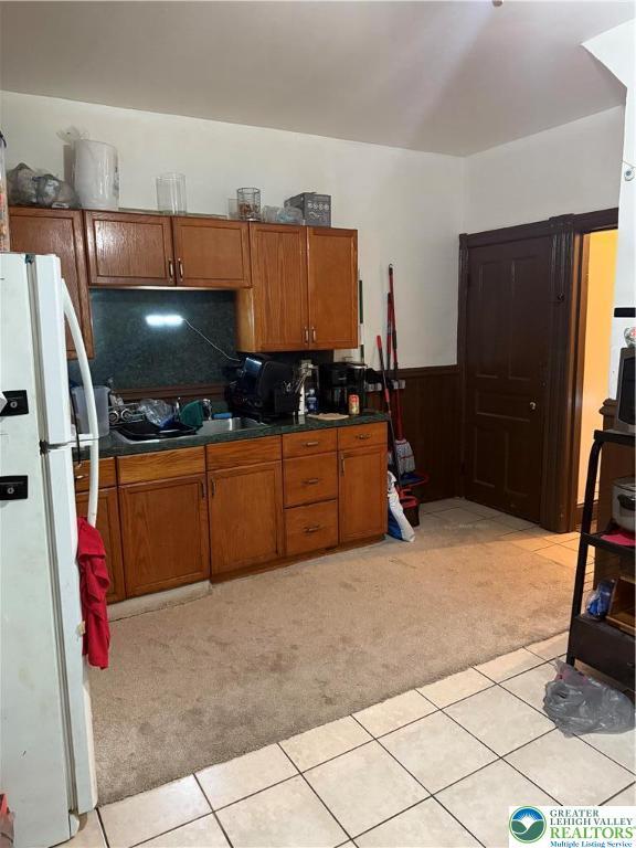 713 E 5th St, Bethlehem City, PA 18015 - kitchen featuring freestanding refrigerator, light colored carpet, brown cabinets, dark countertops, and a wainscoted wall