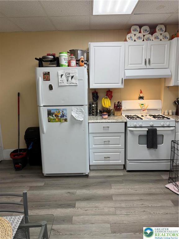 713 E 5th St, Bethlehem City, PA 18015 - kitchen with white appliances, under cabinet range hood, a drop ceiling, white cabinets, and light wood-style floors