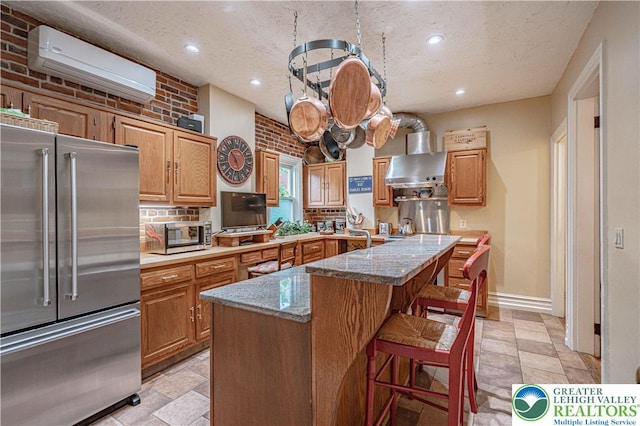 407 N 8th St, Allentown City, PA 18102 - kitchen featuring high end refrigerator, wall chimney exhaust hood, a wall mounted AC, a breakfast bar area, and stone tile floors