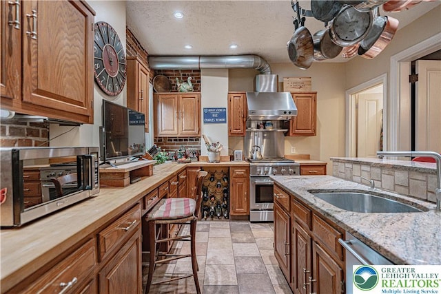407 N 8th St, Allentown City, PA 18102 - kitchen with wall chimney range hood, stainless steel stove, wooden counters, recessed lighting, and brown cabinets