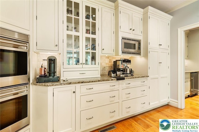 2051 Forge Run, Bethlehem City, PA 18015 - kitchen featuring stainless steel appliances, decorative backsplash, light wood-style floors, glass insert cabinets, and light stone countertops