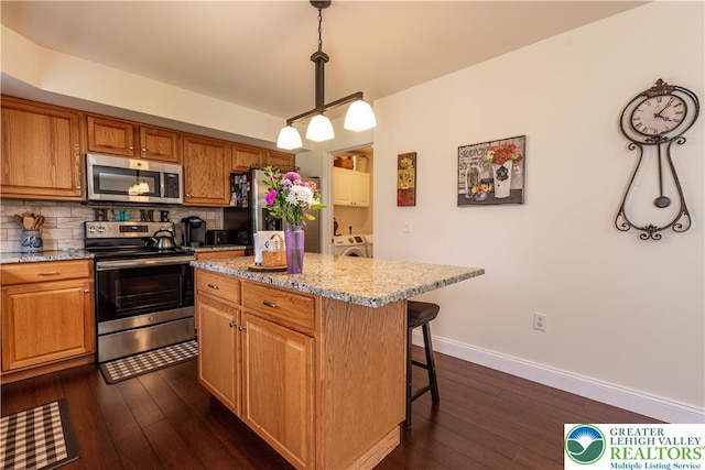 2657 Anthony Ct, Palmer Twp, PA 18045 - kitchen featuring appliances with stainless steel finishes, a breakfast bar area, washer and dryer, backsplash, and dark wood-type flooring