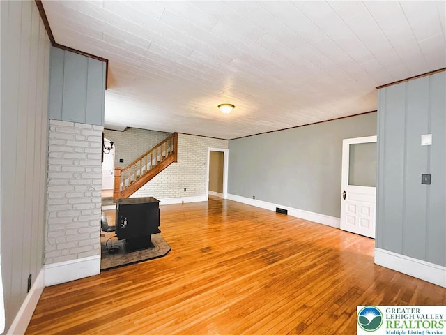233 Lafayette Ave, Palmerton Boro, PA 18071 - unfurnished living room with hardwood / wood-style flooring, brick wall, a wood stove, ornamental molding, and stairway
