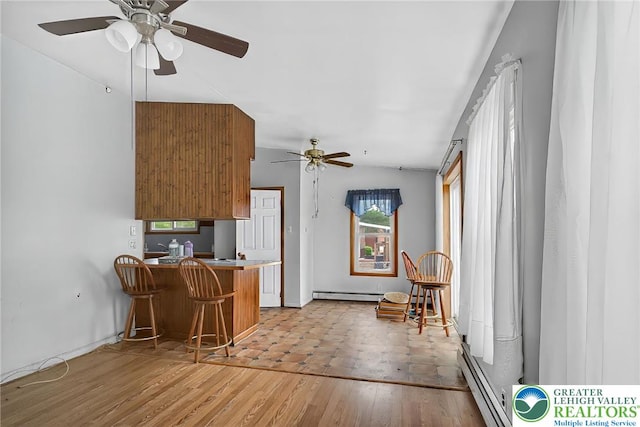 815 Summit Ave, Prospect Park, PA 19076 - kitchen featuring baseboard heating, ceiling fan, a peninsula, light wood finished floors, and a kitchen bar