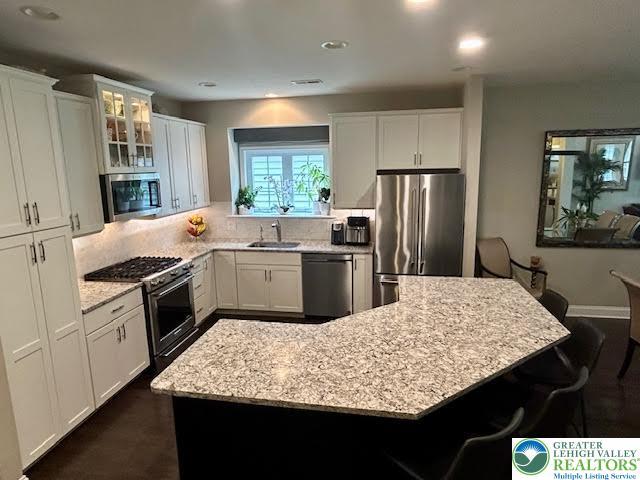 1051 Resolution Dr, Hanover Twp, PA 18017 - kitchen featuring appliances with stainless steel finishes, decorative backsplash, light stone counters, white cabinetry, and glass insert cabinets