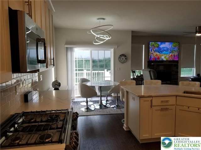3583 Daylily Dr, Upper Milford Twp, PA 18049 - kitchen with stainless steel microwave, a fireplace, dark wood-type flooring, tasteful backsplash, and open floor plan