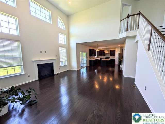 237 Danbury Dr, Upper Nazareth Twp, PA 18064 - unfurnished living room with a high ceiling, healthy amount of natural light, dark wood-type flooring, stairway, and a fireplace with flush hearth