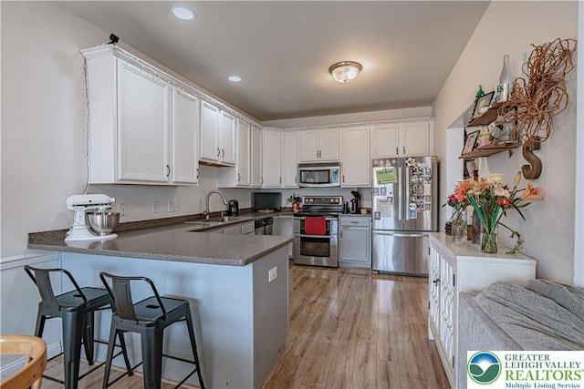 301 Maple Ct, Alburtis Boro, PA 18011 - kitchen featuring appliances with stainless steel finishes, a peninsula, white cabinetry, light wood-style floors, and a kitchen bar