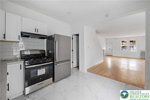 907 N 5th St, Allentown City, PA 18102 - kitchen featuring appliances with stainless steel finishes, under cabinet range hood, radiator heating unit, decorative backsplash, and white cabinetry