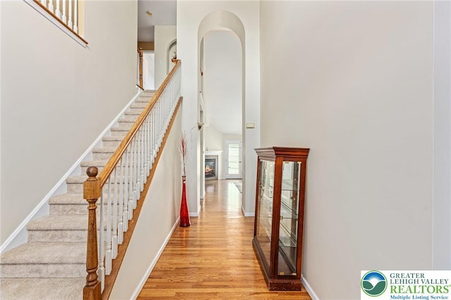 441 Sawgrass Dr, Upper Macungie Twp, PA 18104 - staircase featuring wood finished floors, a towering ceiling, and a glass covered fireplace