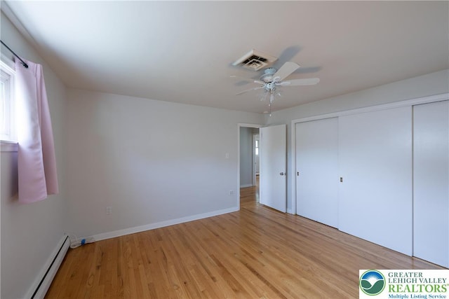 unfurnished bedroom featuring a baseboard radiator, light wood finished floors, a closet, and ceiling fan