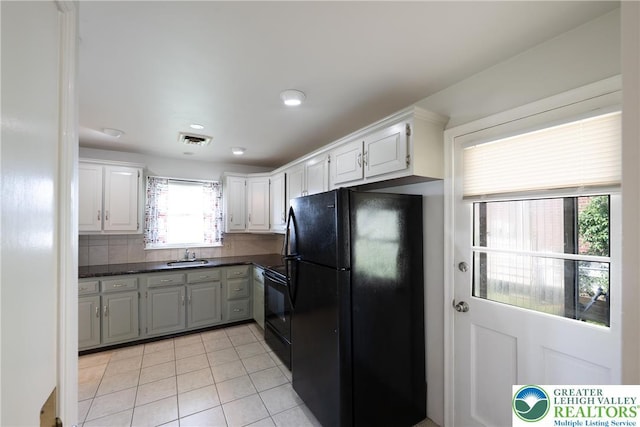 kitchen featuring freestanding refrigerator, dark countertops, light tile patterned floors, stove, and white cabinetry