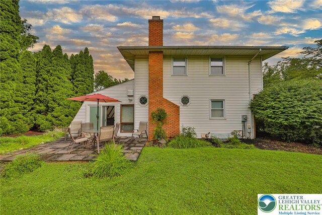 1812 Treeline Dr, Forks Twp, PA 18040 - back of property at dusk with a patio, a chimney, and a lawn