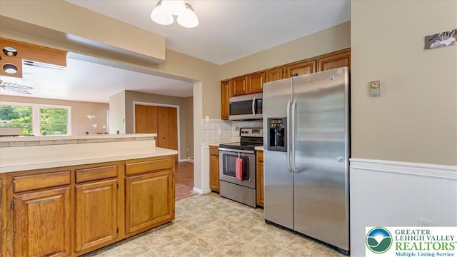 671 Dotters Corner Rd, Polk Twp, PA 18058 - kitchen featuring stainless steel appliances, light countertops, brown cabinets, decorative backsplash, and a wainscoted wall