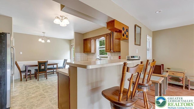 671 Dotters Corner Rd, Polk Twp, PA 18058 - kitchen with freestanding refrigerator, brown cabinetry, a peninsula, a chandelier, and light countertops
