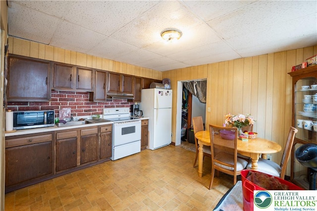 638 N 16th St, Allentown City, PA 18102 - kitchen with white appliances, under cabinet range hood, wood walls, light countertops, and brick patterned floors