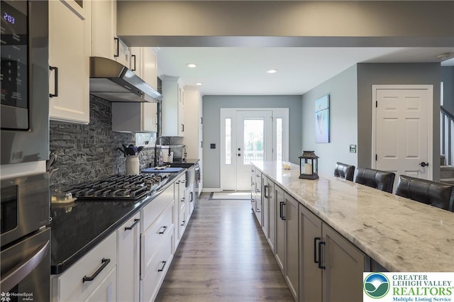 3536 New Hampshire Ave, Bethlehem Twp, PA 18045 - kitchen featuring appliances with stainless steel finishes, under cabinet range hood, dark wood-type flooring, light stone counters, and decorative backsplash