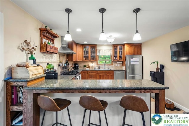1079 Marshalls Creek Rd, Middle Smithfield Twp, PA 18302 - kitchen featuring stainless steel appliances, wall chimney range hood, brown cabinetry, decorative backsplash, and a peninsula