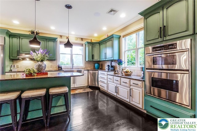 4260 W Wyndemere Cir, Lowhill Twp, PA 18078 - kitchen featuring stainless steel appliances, green cabinets, ornamental molding, decorative backsplash, and a kitchen breakfast bar