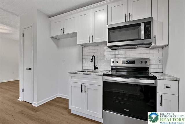 182 Maxatawny Dr, Coolbaugh Twp, PA 18347 - kitchen featuring appliances with stainless steel finishes, light wood-type flooring, decorative backsplash, white cabinetry, and light stone countertops