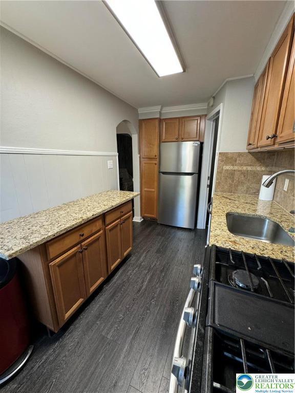 449 E Garrison St, Bethlehem City, PA 18018 - kitchen with freestanding refrigerator, range with gas stovetop, arched walkways, brown cabinetry, and wainscoting