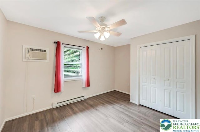 5117 Hounds Ear Rd, Coolbaugh Twp, PA 18466 - unfurnished bedroom featuring baseboard heating, an AC wall unit, wood finished floors, a closet, and a ceiling fan