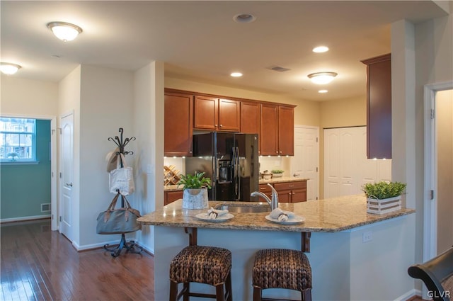 kitchen with a breakfast bar, dark hardwood / wood-style flooring, black fridge with ice dispenser, stone counters, and sink