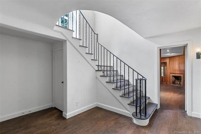 staircase featuring dark wood-type flooring and a brick fireplace