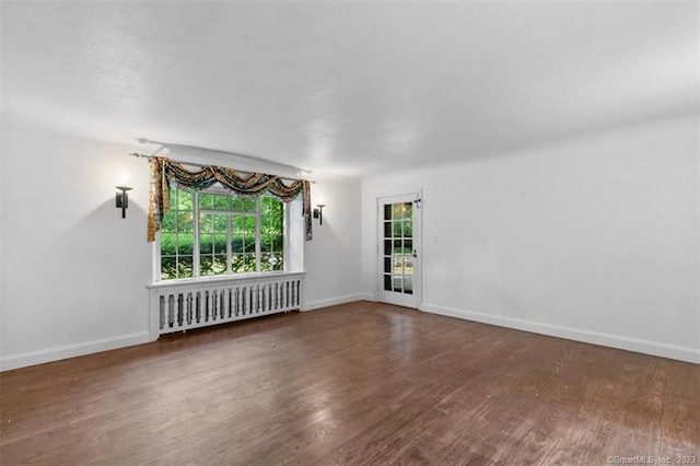 empty room with dark wood-type flooring, radiator heating unit, and a wealth of natural light