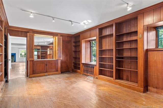 interior space featuring rail lighting, wood walls, built in shelves, and light hardwood / wood-style flooring