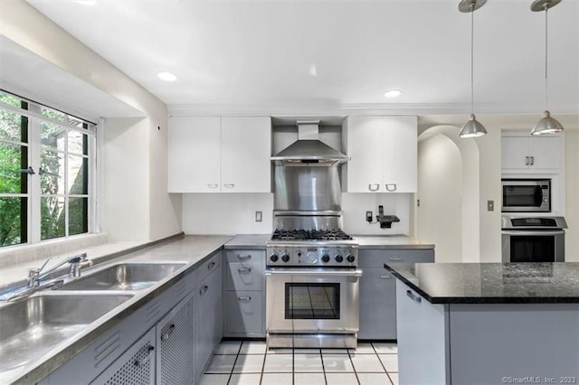 kitchen with appliances with stainless steel finishes, light tile floors, decorative light fixtures, gray cabinets, and wall chimney exhaust hood